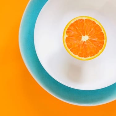 An orange slice on a plate atop an orange-colored backdrop